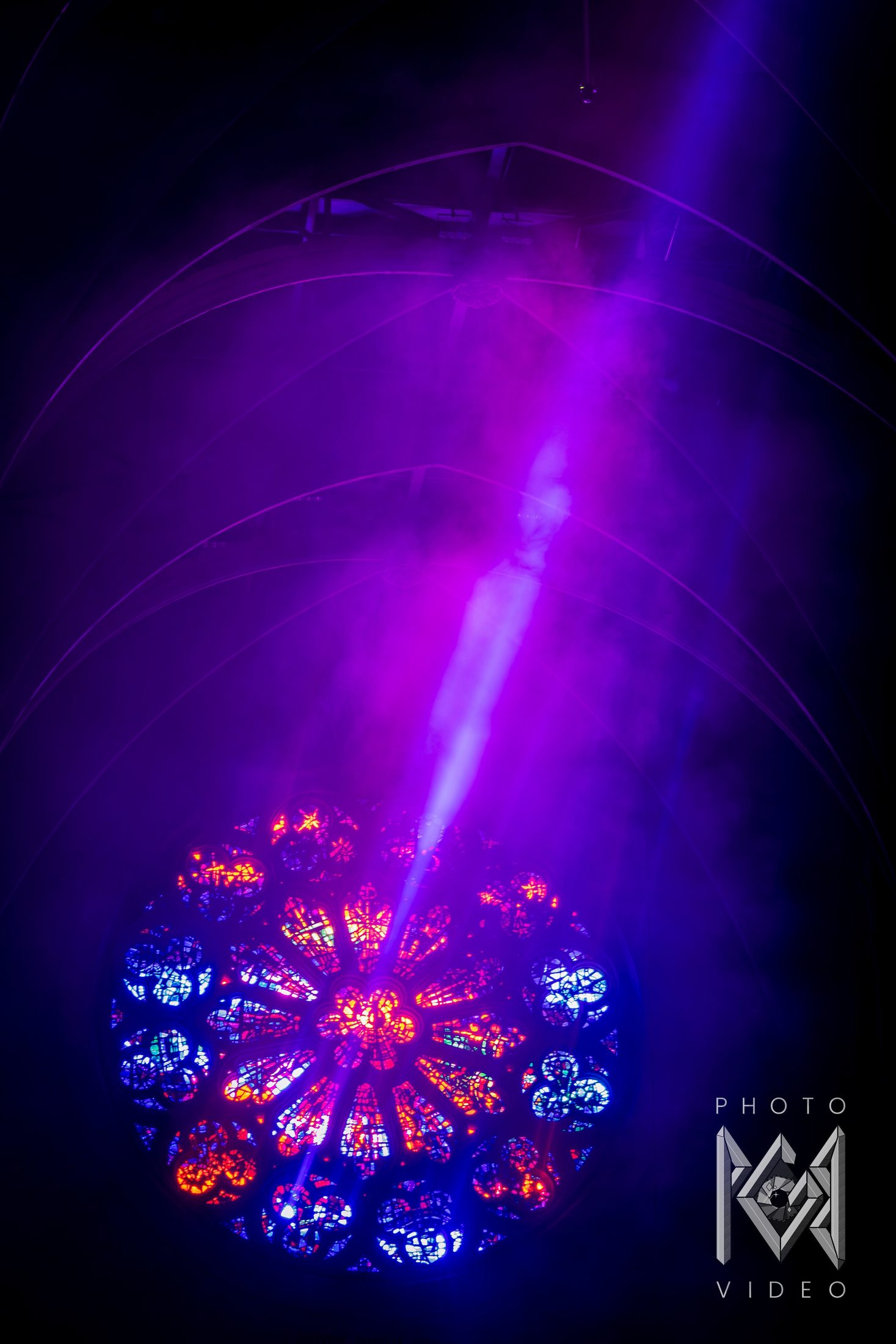 A violet beam of light cutting through haze toward a glowing rose window high in a dark cathedral vault