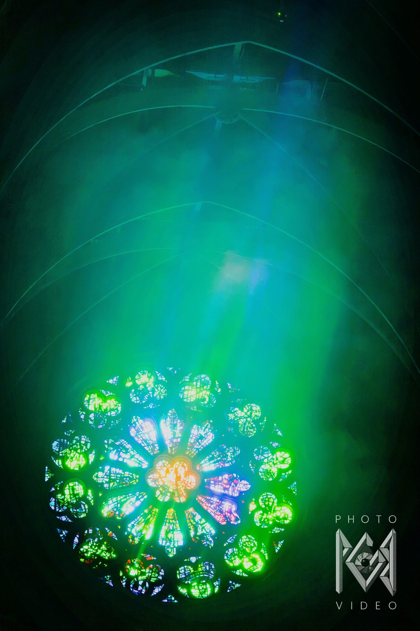 Green haze and beams of light filling a cathedral vault above a rose window glowing green, gold and blue