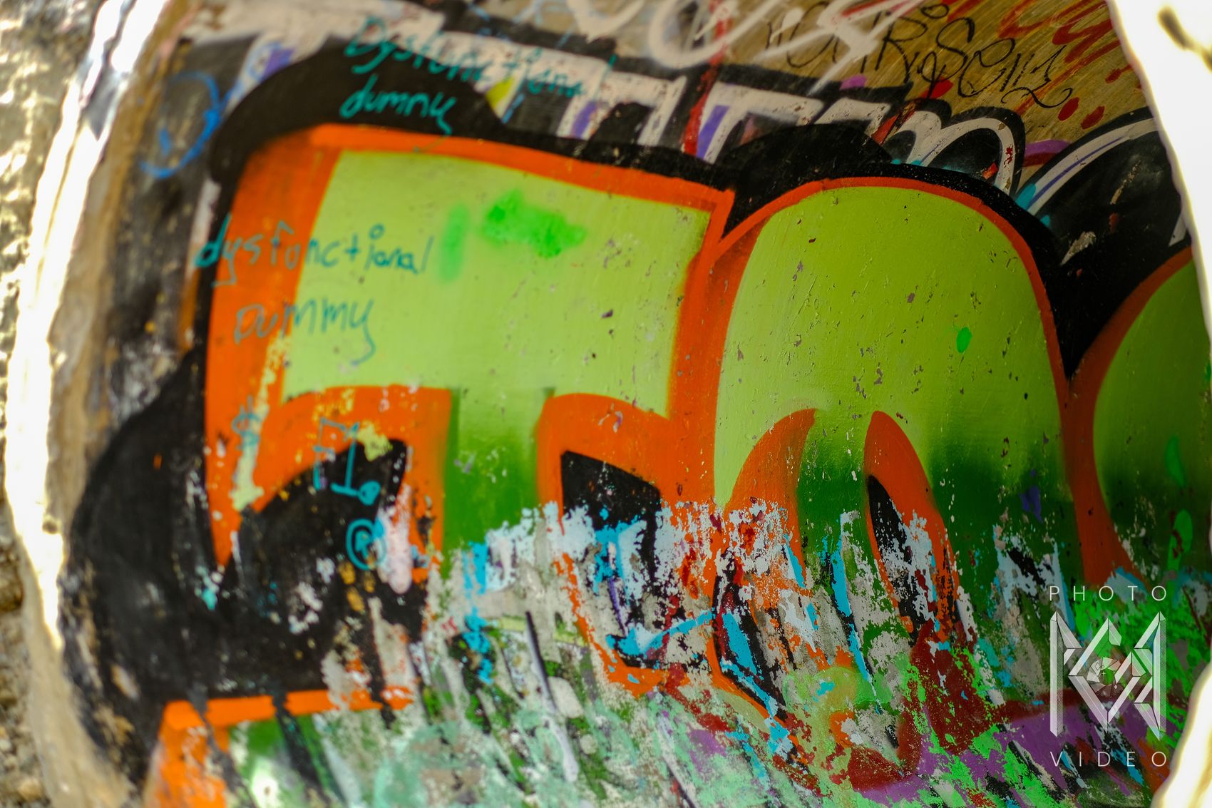 Layers of bright green, orange and black graffiti covering the curved inside of a concrete wall