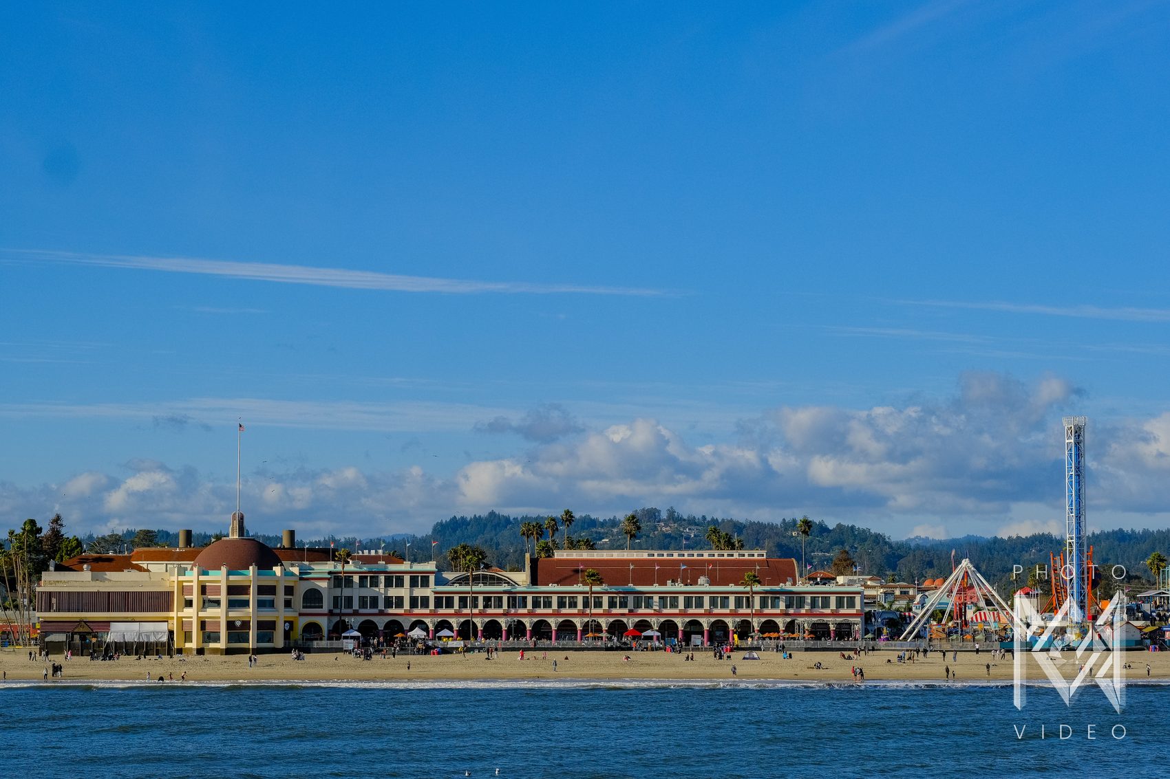 The historic casino building and its arcade of arches along the beach, with a drop tower and rides to the right under a deep blue sky