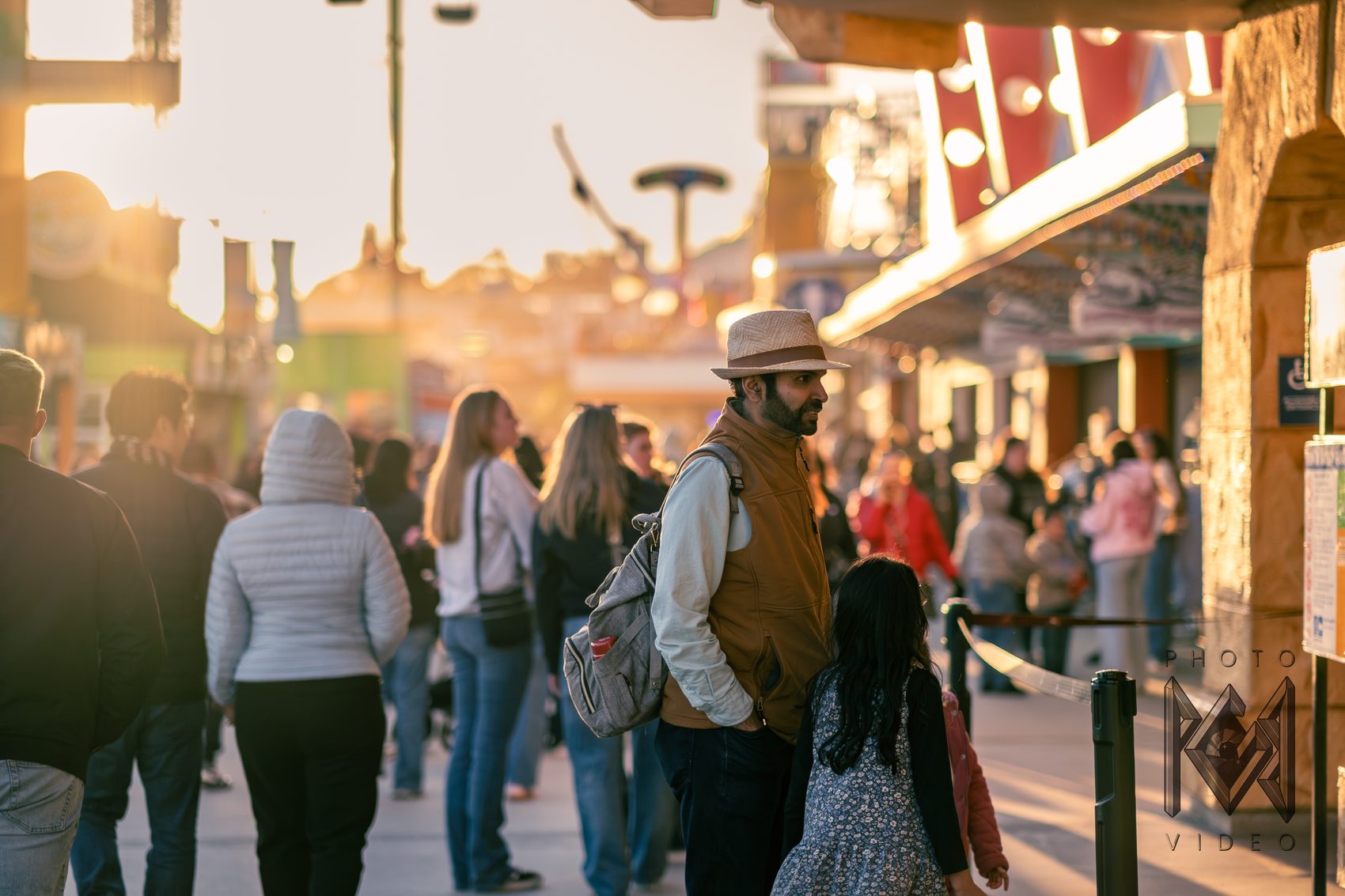A man in a straw hat and a young girl watching the crowd on the boardwalk in warm, glowing evening light