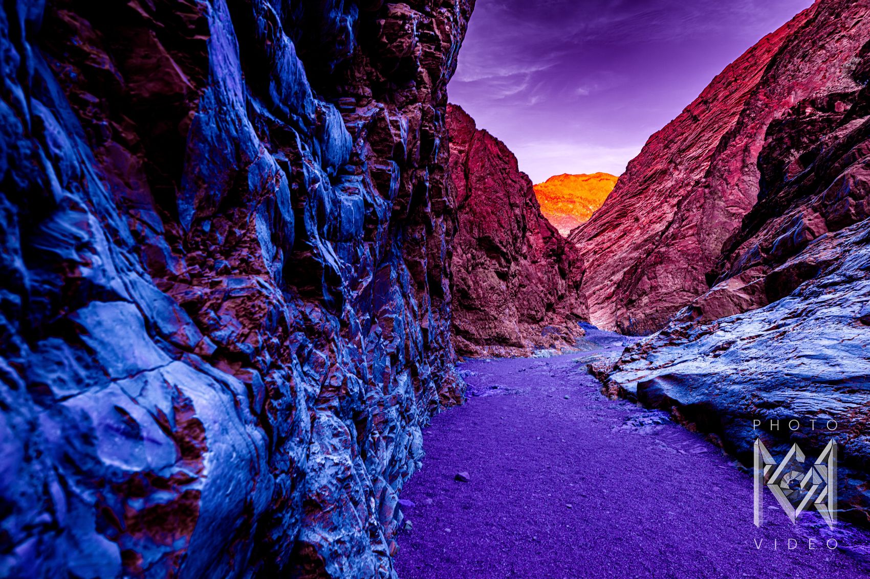 A narrow slot canyon in electric blue and violet leading to a glowing orange peak