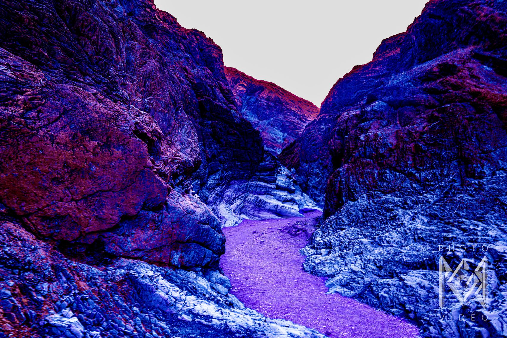 Canyon walls in deep blue, red and violet closing in around a lilac gravel wash