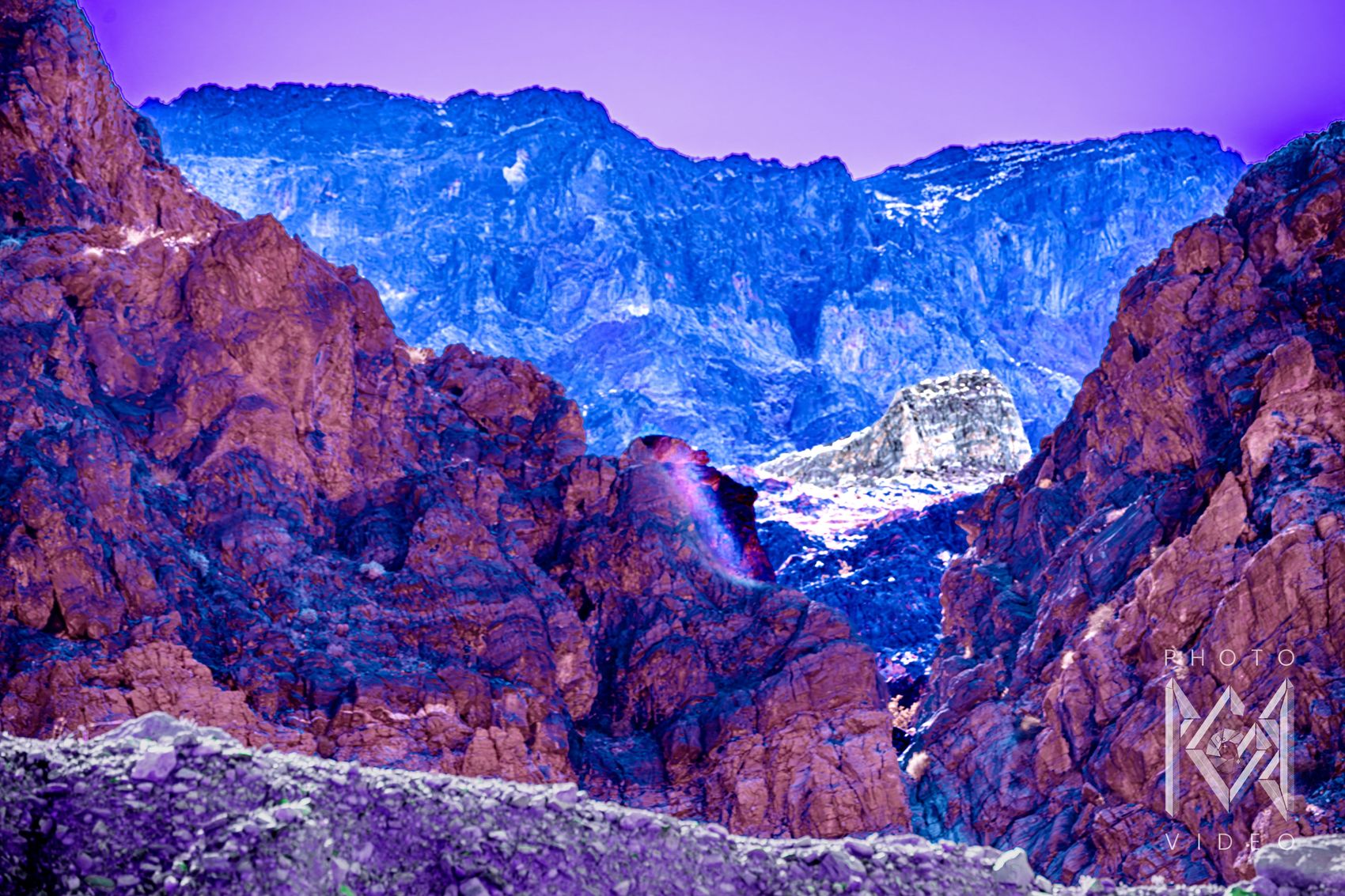 Rose and plum canyon walls framing a range of icy blue mountains under a lavender sky