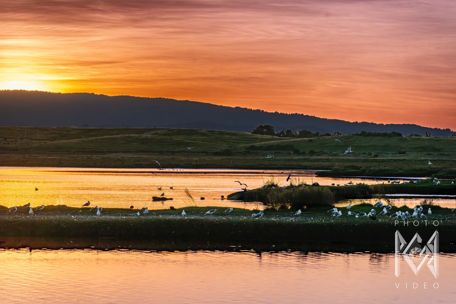 The marsh at sunset, its channels mirroring an orange and violet sky above low hills