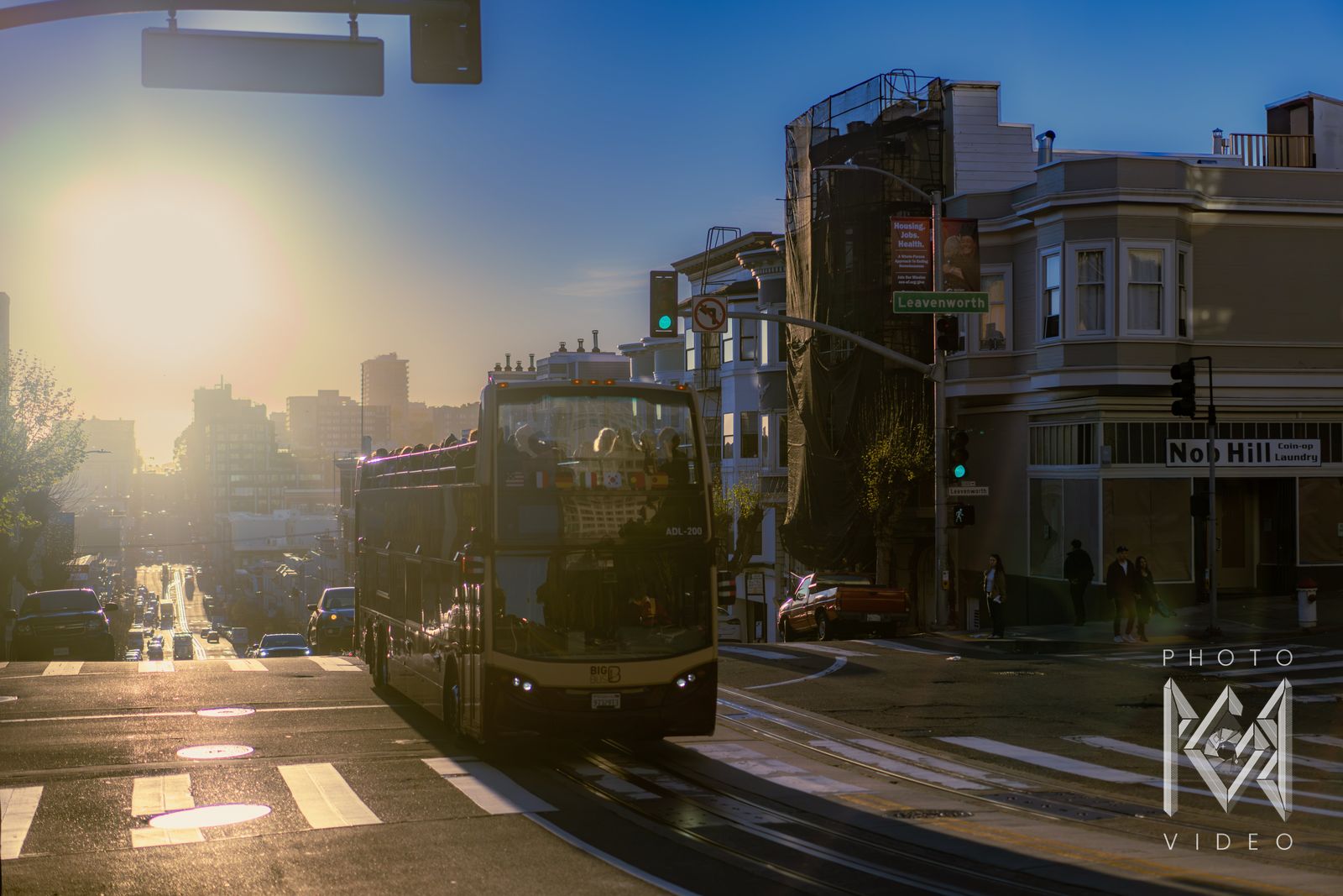 An open-top double-decker bus climbing toward the low sun at a Nob Hill corner, cable car tracks gleaming in the road