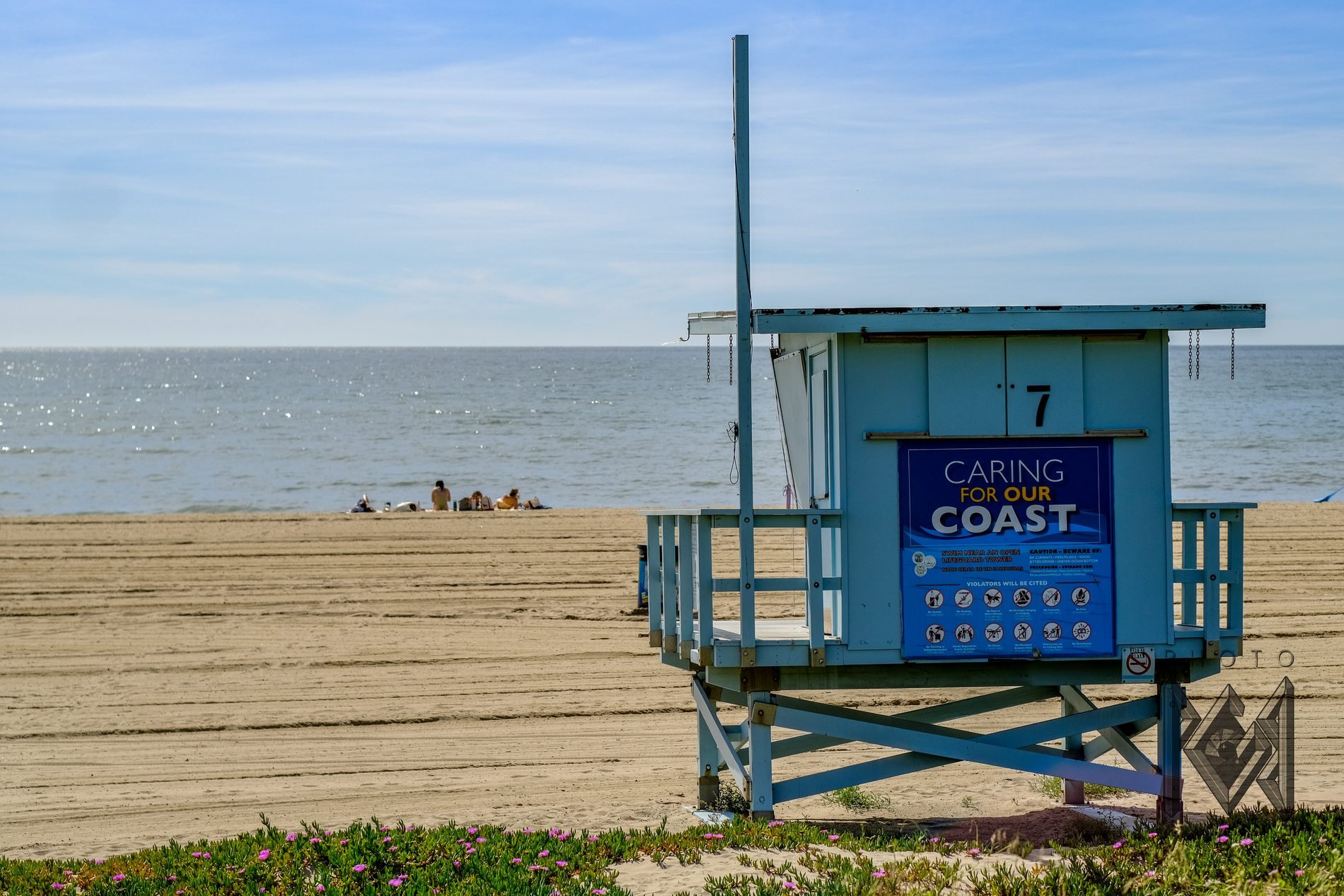 Lifeguard tower 7 on a wide sandy beach with its blue Caring for our Coast sign, the ocean beyond