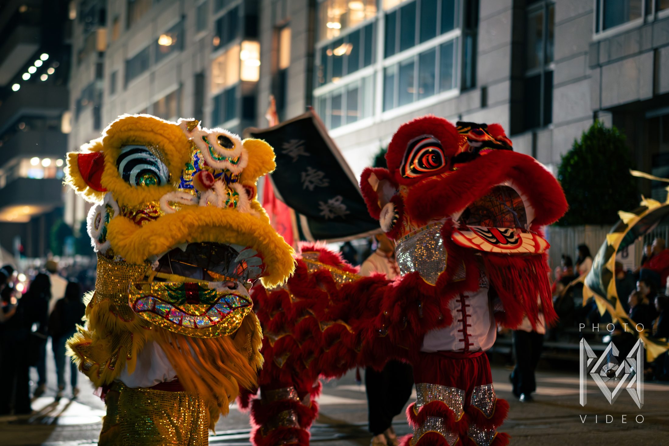 A golden lion and a red lion dancing side by side in a night street parade, their fur and sequins glowing under the streetlights