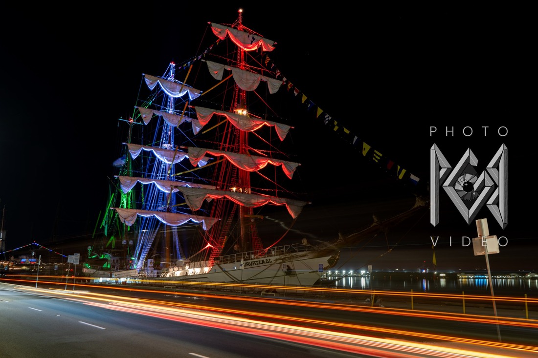 The ship's masts lit in red, white and blue above long light trails on a road