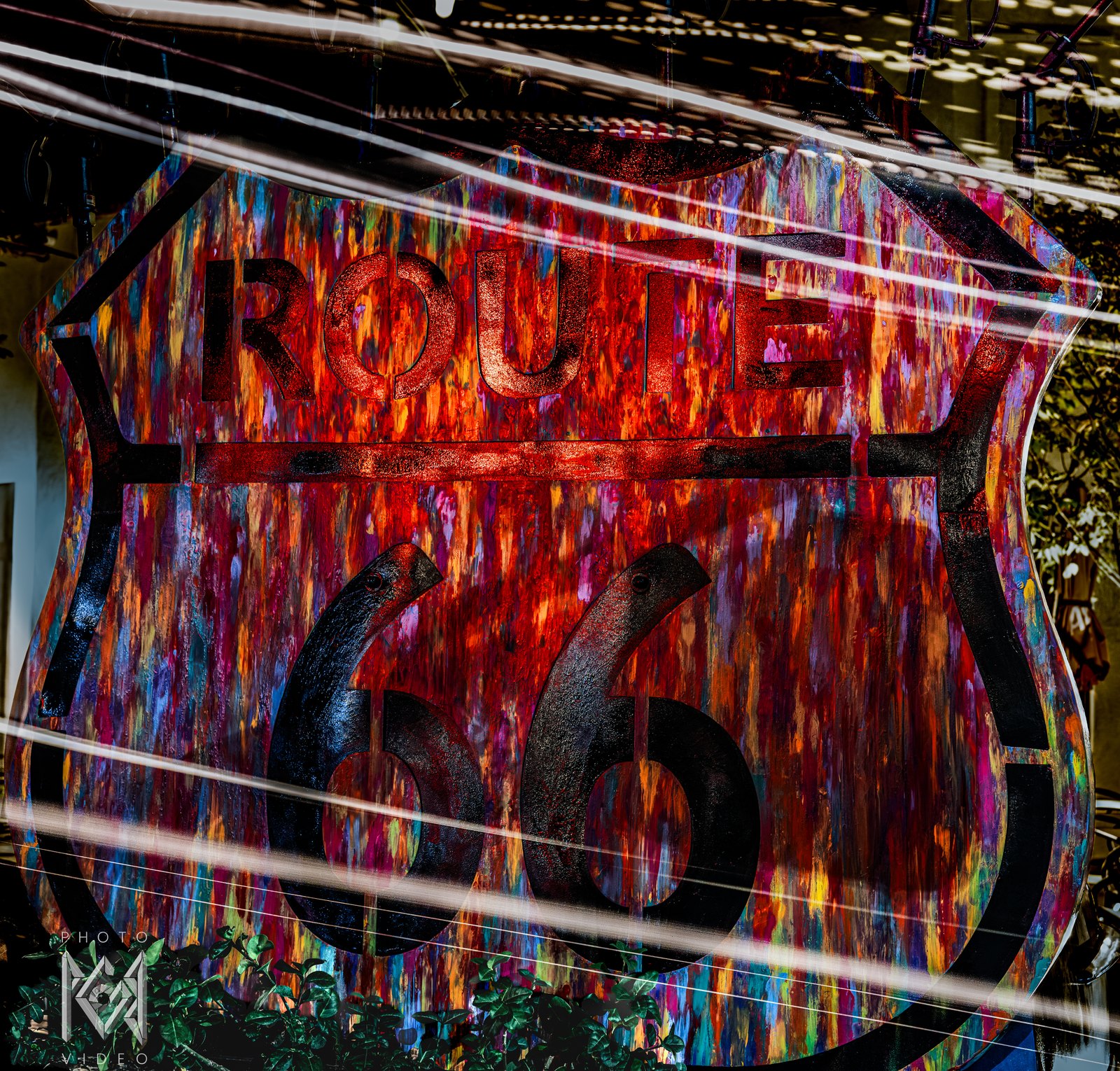 A painted Route 66 shield sign in red, orange and blue brushstrokes, crossed by long streaks of light